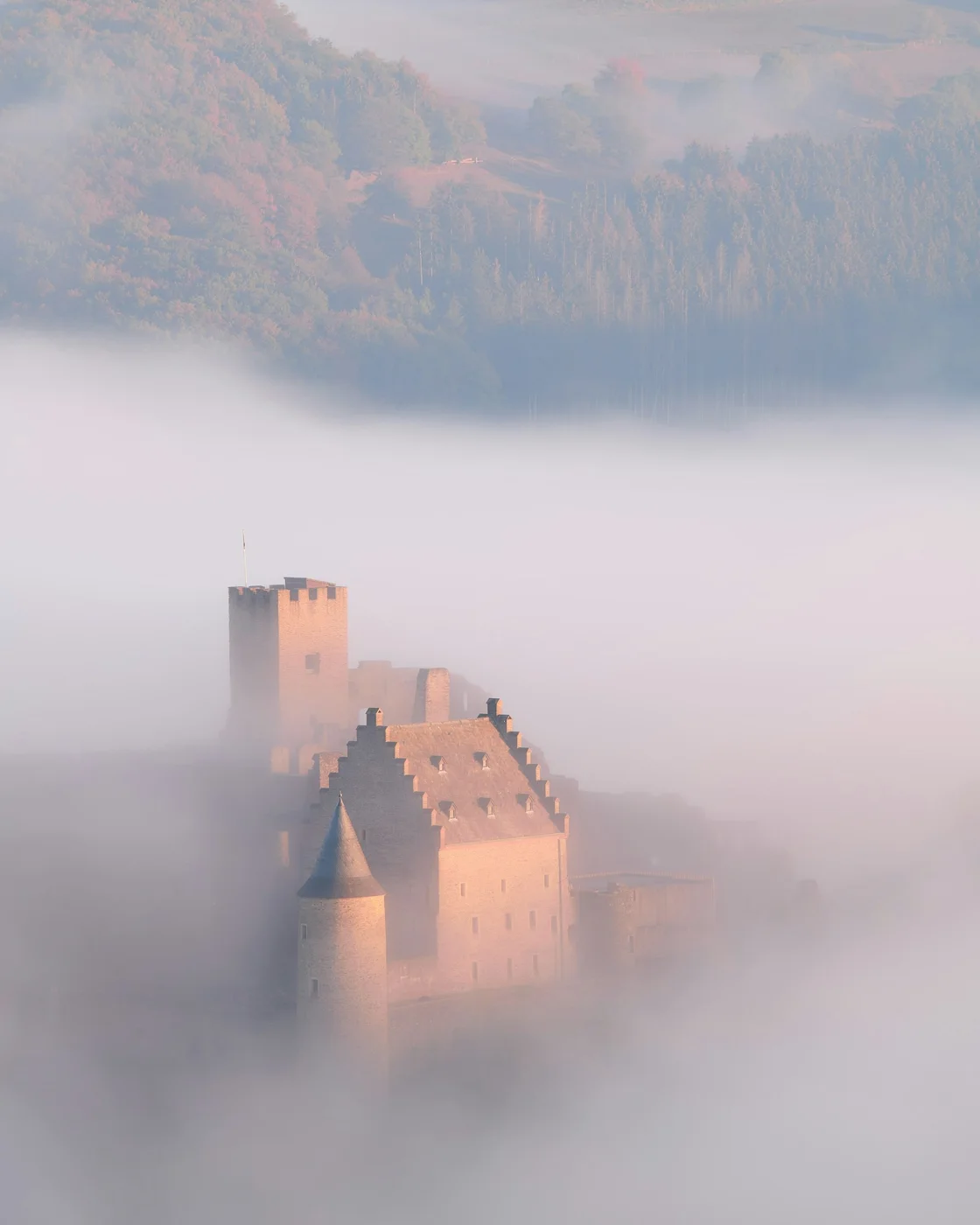 Bourscheid Castle emerging above low valley mist